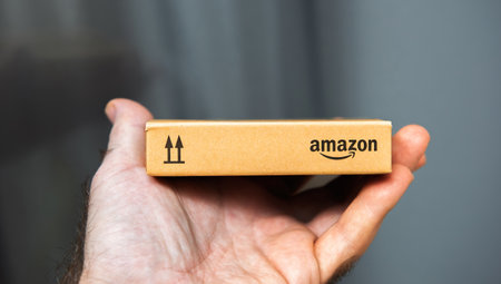 Paris, France - Nov 22, 2021: Close-up of a hand holding a small Amazon-branded cardboard package, showcasing the compact size and minimalist packaging design in a clean background settingのeditorial素材