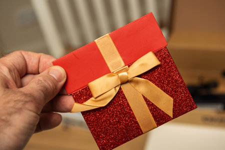 A sparkly red gift card holder with a golden bow, held in hand, showcasing festive and elegant design.の写真素材