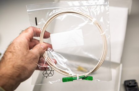 Hand holding a fiber optic cable sealed in a transparent plastic bag with green connectors, showcasing packaging and product designの写真素材