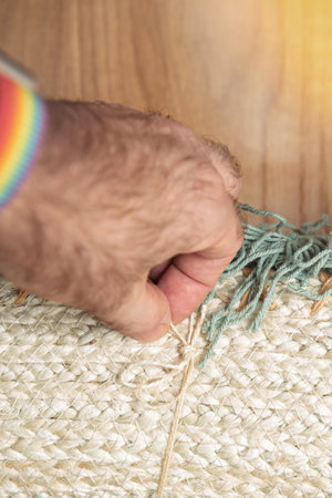 Close-up of a hand tying a knot in natural woven fabric with colorful yarn accents, placed on a wooden floor.の写真素材