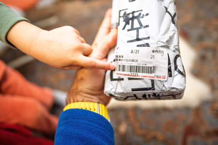 Paris, France - Dec 7, 2024: A child hand points to the shipping label of a wrapped package, emphasizing curiosity and interaction in an everyday momentのeditorial素材