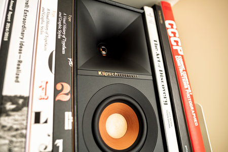 Paris, France - Apr 18, 2023: A compact black and gold Klipsch Reference speaker displayed alongside an assortment of graphic design and photography books, neatly organized on a modern white bookshelfのeditorial素材