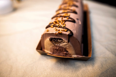 A chocolate Yule log partially sliced to reveal creamy chocolate layers and a rich filling, decorated with caramelized nuts and icing drizzlesの写真素材