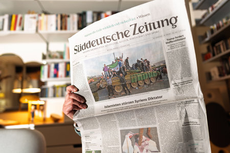 Paris, France - Dec 9, 2024: Person holding newspaper with a headline about the overthrow of Syria dictator, set in a modern, well-lit interiorのeditorial素材