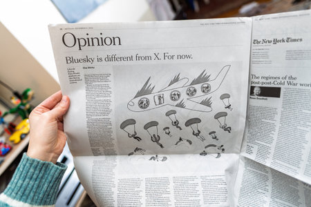 Paris, France - Dec 9, 2024: Person reading a New York Times opinion piece comparing Bluesky and X, accompanied by an illustration of a damaged airplane with parachuting passengersのeditorial素材