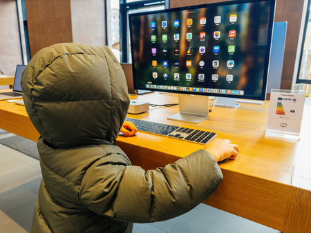 Paris, France - Dec 10, 2024: A child in a green jacket interacts with an Apple Studio Display and Mac Mini in a store, exploring technology and engaging with the sleek interface.のeditorial素材