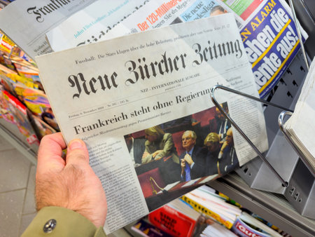 Berlin, Germany - Dec 6, 2024: A person holding the Neue Zuricher Zeitung newspaper at a newsstand, featuring prominent international headlines and surrounded by colorful magazine covers.のeditorial素材