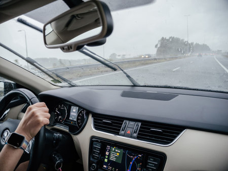 Den Helder, Netherlands - Aug 24, 2024: Interior shot of a car on a rainy highway, showing a driver hand on the steering wheel and windshield wipers in motion for visibility - carplay from apple computers on the dashboardのeditorial素材