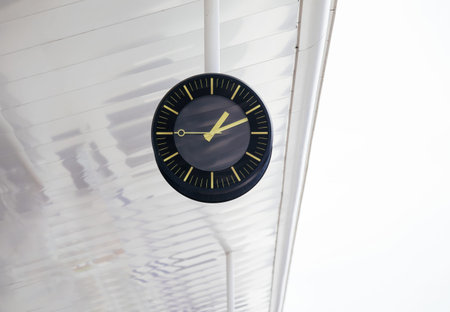 A modern black clock with yellow markings is suspended from a white ceiling