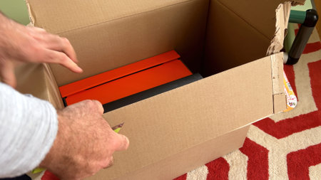 A hand is seen meticulously unboxing a smaller orange and black cardboard from within a larger...