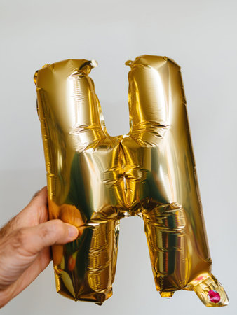 A male hand showcases the letter H, crafted from gold helium balloons. It gleams prominently against...