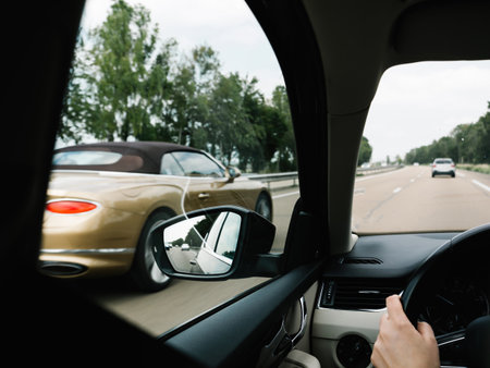 A French freeway bustles with activity as a woman's hand firmly holds her steering wheel. A champagne-hued convertible enhances the upscale scene.の写真素材