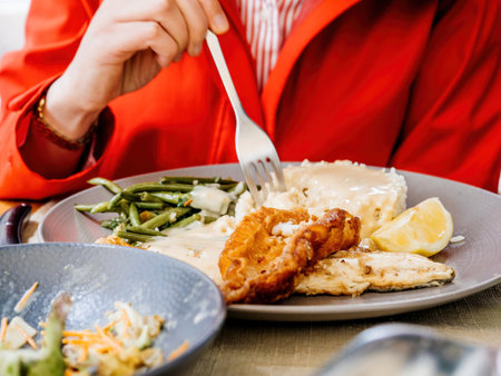 Person in red coat eating fish with lemon and rice using a fork, on an outdoor terrace of a restaurantの写真素材