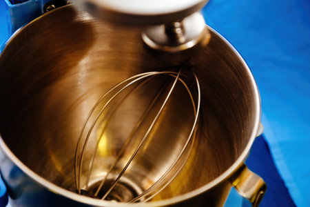 A clean mixer bowl and its metallic attachments sit against a vibrant blue background, ready for the next culinary adventureの写真素材