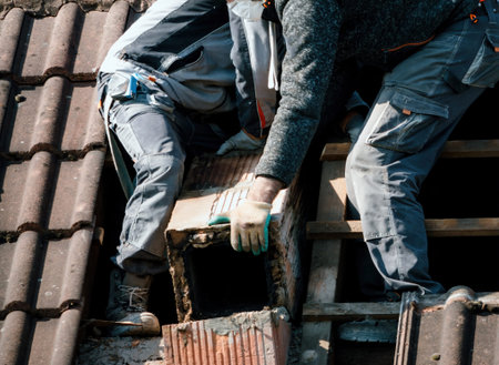 Dedicated male workers on the rooftop meticulously dismantle a brick chimney during a comprehensive home renovation project.の写真素材