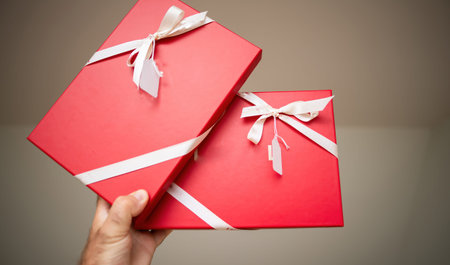 A masculine hand grasps a two red striking, crimson gifts, meticulously enveloped in the soft caress...