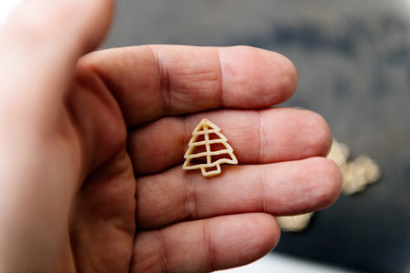 A hand presenting a tree-shaped pasta piece, showcasing its festive design and intricate details for...