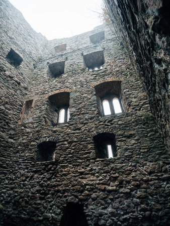 Towering stone walls of an abandoned castle with multiple arched windows under an overcast sky, emanating a hauntingly mysterious and desolate vibe.の写真素材