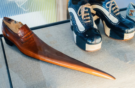 A historical brown leather shoe with an exaggerated elongated toe, displayed alongside a pair of black and white platform shoesの写真素材