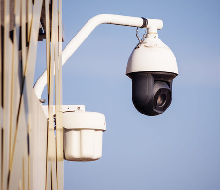 A white dome-shaped security camera with a black lens is attached to a metal arm on the side of a...