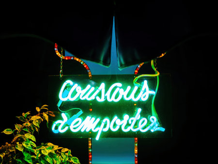 Vibrant neon sign reading Couscous a emporter transalted Couscous to go - glows brightly in the night, adorned with decorative lights and foliage.の写真素材