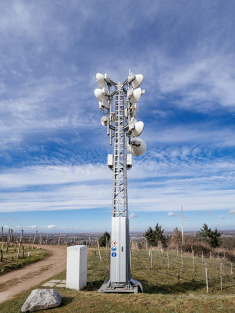 A telecommunications tower equipped with multiple antennas stands in a vineyard, ensuring data transmission over the rural landscape and nearby villages.の写真素材