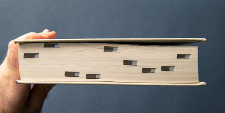 A hand holds a thick book, viewed from the side showing cut-out tabs for easy chapter access,...