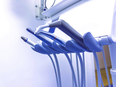 Close-up view of several dental handpieces attached to a unit inside a brightly lit dental clinic, with focus on the metallic textures and curved instrument holdersの写真素材