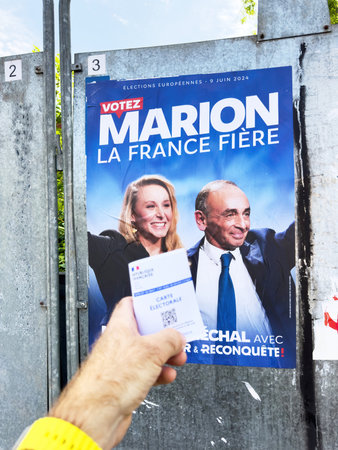 Paris, France - Jun 9, 2024: A person holds a French carte electorale in front of a political campaign poster for the 2024 European elections featuring Marion Marechal and Eric Zemmour on a public display boardのeditorial素材
