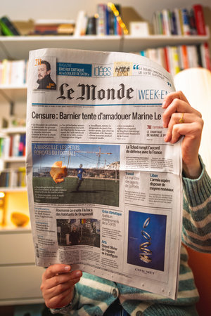 Paris, France - Dec 9, 2024: A person in a striped sweater is reading the weekend edition of Le Monde newspaper at home, with visible headlines about politics, football in Marseille, and international affairsのeditorial素材