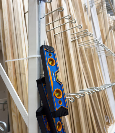 Paris, France- Mar 27, 2025: Three blue and orange Dexter spirit levels are zip-tied to a white metal display frame among rows of wooden trim boards in a hardware or home improvement storeのeditorial素材