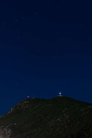 Clear, starry night with lighthouse on top of a mountainの写真素材