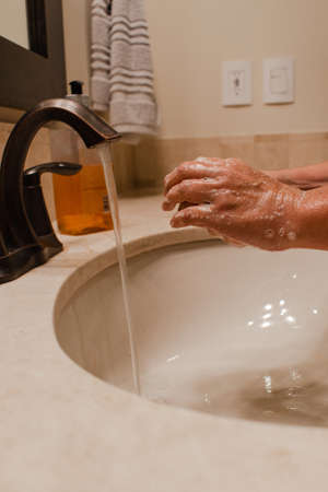 Person washing hands with soap on a bathroom sink with running waterの写真素材