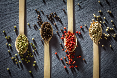 slate tray with wooden spoons with four types of pepper, green, black, pink and whiteの写真素材