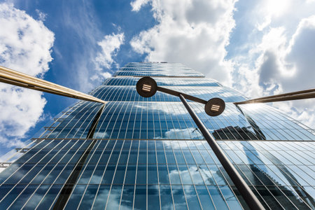 A towering glass skyscraper rises dramatically into the sky, its reflective surface mirroring soft...