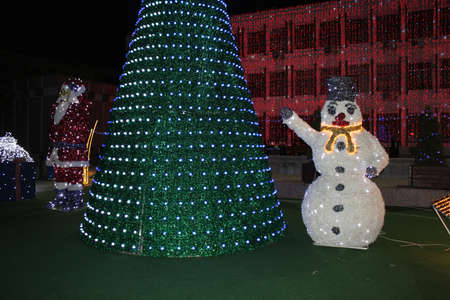 Snowman with a lot of lights near a Christmas Treeの写真素材