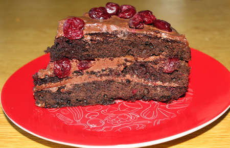 Black Forest (or Foret Noir) cake with brown cream and sour cherries on a red plateの写真素材