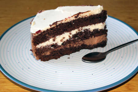 A piece of cake with white and brown cream on a blue circles plate and with a spoonの写真素材