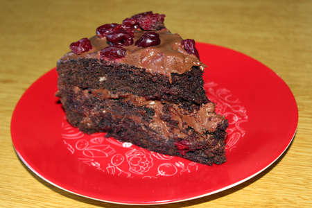 Black Forest (or Foret Noir) cake with brown cream and sour cherries on a red plateの写真素材