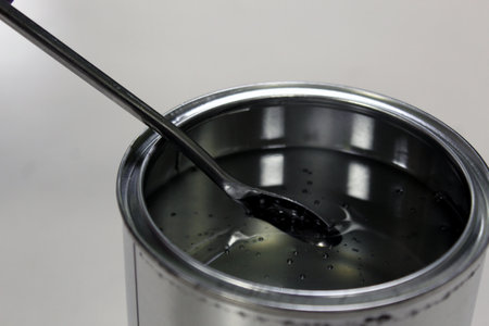 Technician weighing transparent epoxy resin for a paint in a can on a balance by spatula on white backgroundの写真素材