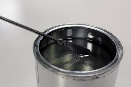 Technician weighing transparent epoxy resin for a paint in a can on a balance by spatula on white backgroundの写真素材