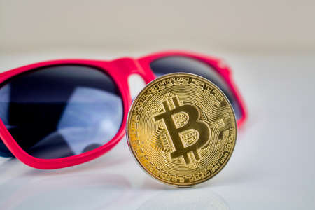 Cryptocurrency physical gold bitcoin coin and pink sunglassesのeditorial素材
