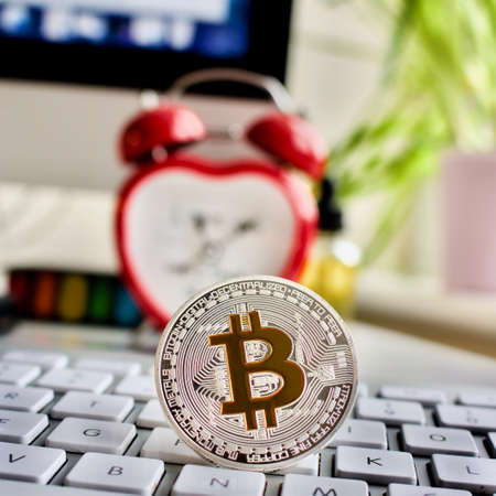 Cryptocurrency physical silver bitcoin coin, keyboard, screen and clock.のeditorial素材