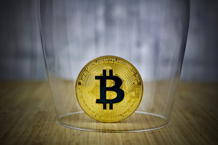 Cryptocurrency physical gold bitcoin coin with black sign protected by glass.