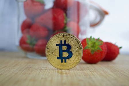 Cryptocurrency physical gold bitcoin coin. Red strawberries concept.のeditorial素材