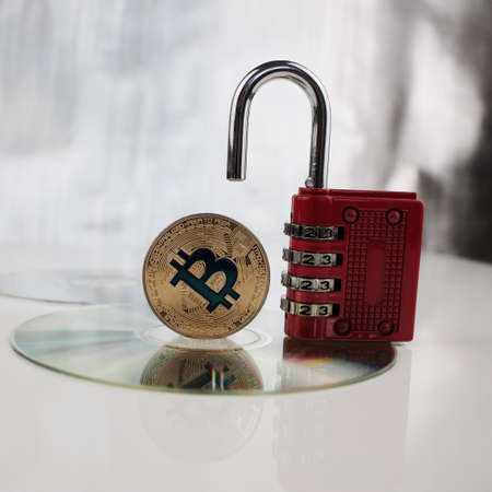 Digital currency physical gold bitcoin near red padlock on the CDの写真素材