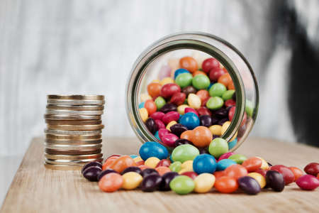 Money jar and colorful sweets on the wooden board in the kitchen.の写真素材