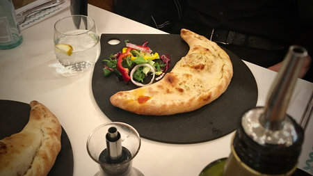 Fresh vegetables and big pizza dumpling on black plate in restaurant.