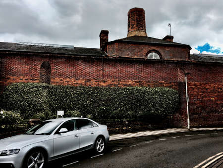 Old prison in town centre near silver car and brickwall.の写真素材