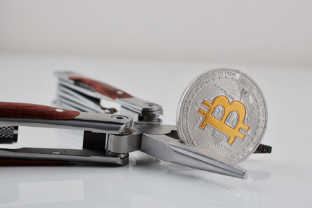 Digital currency physical silver bitcoin coin . Yellow sign "b" and pocket knife on the table.の写真素材